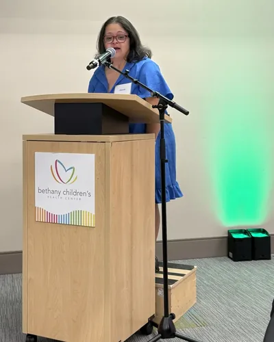 Danielle speaking into a microphone at a podium marked Bethany Children's Health Center.